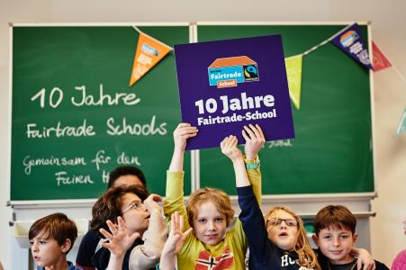 Titelbild 10 Jahre Fairtrade-Schools. Schüler*innen halten ein Schild mit dem Logo. Quelle: Fairtrade Deutschland e.V. / Tobias Thiele