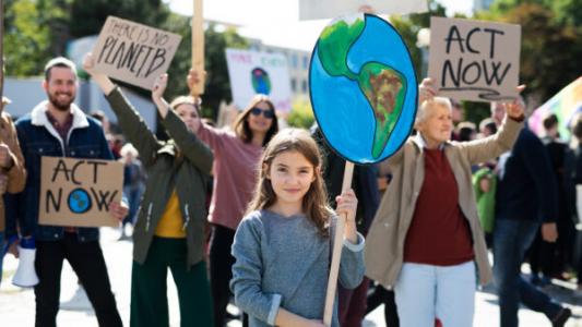 Demonstrierende Menschen mit Schildern, auf denen z.B. Act Now steht, im Vordergrund ein Kind mit Plakat, auf dem die Erde abgebildet ist. Bild von Shutterstock